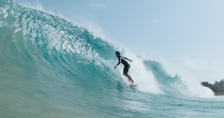 A surfer is riding a big blue wave and gets in the barrel