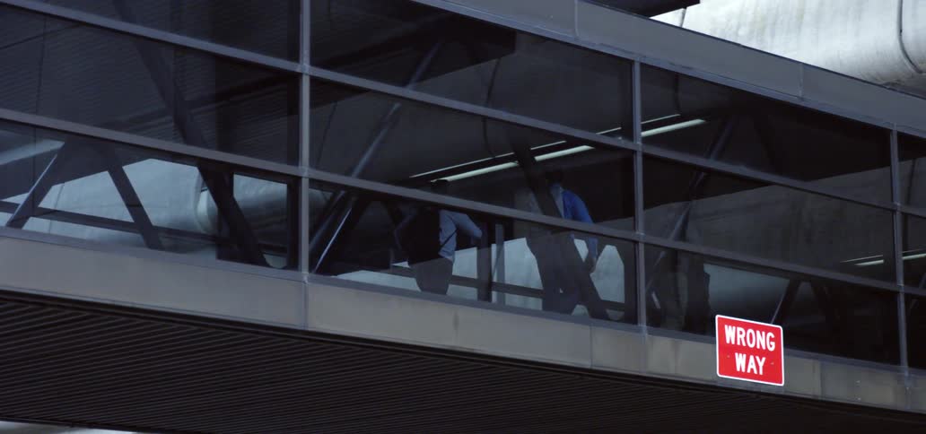 A group of men walk along an enclosed bridge during the day