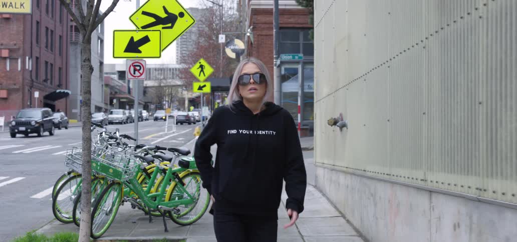 Blonde woman with glasses black sweater and jeans uses smartphone and walks down the street in the city