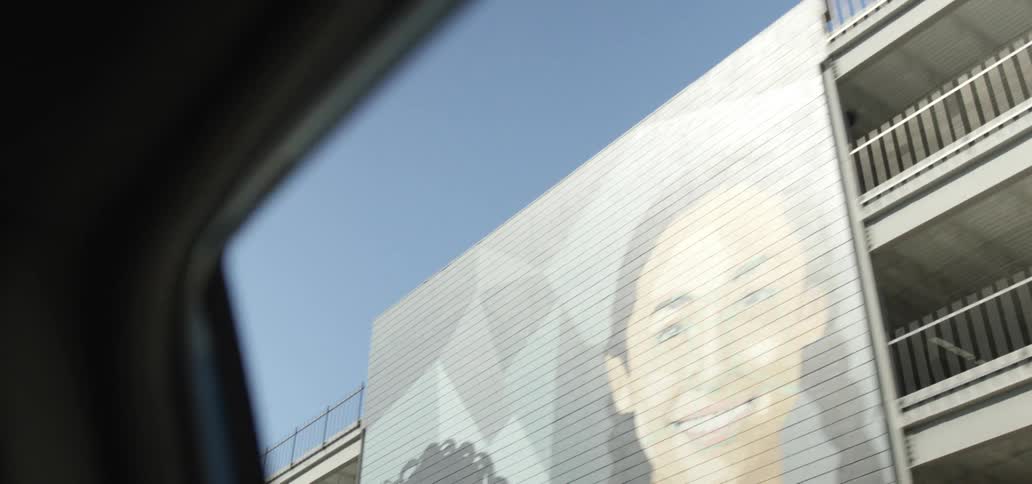 A car driving by city buildings and a large mural