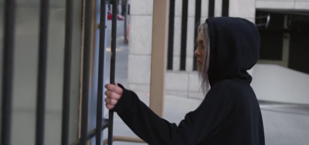 A woman wearing a hoodie with hood up looks back over her shoulder as she walks toward the street
