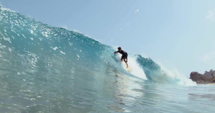 Male surfer with black wetsuit rides on ocean wave on surfboard