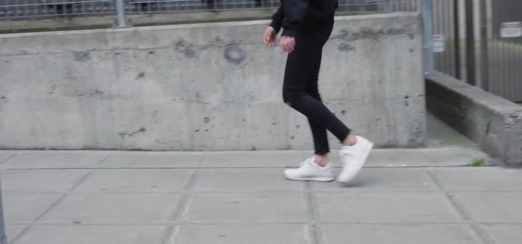 Young woman wearing a black hoodie walking down the sidewalk of a big city