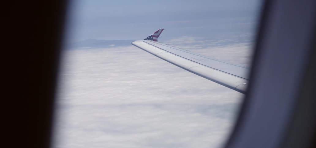 View out of an airplane window of the wing and clouds below