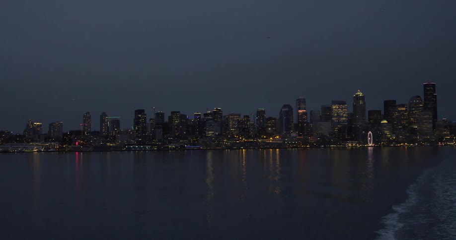 City skyline with illuminated skyscrapers seen from moving boat at night