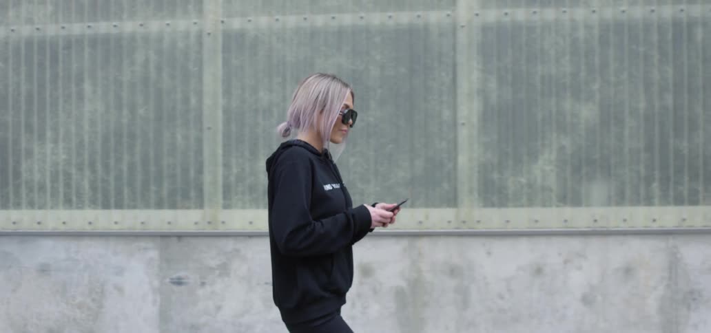 A woman walking outside on a sidewalk with a smartphone in hand