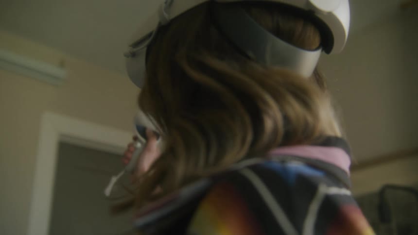 A teenage girl is wearing virtual reality goggles and holding the controllers as she moves her arms playing a game