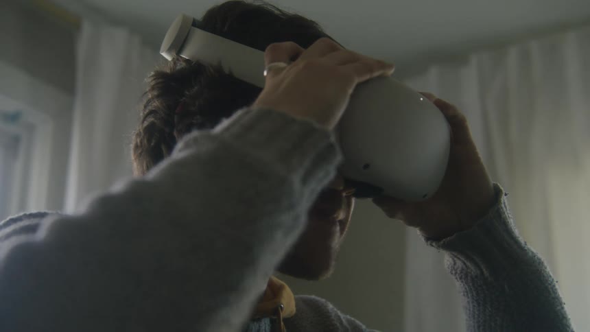 Man with gray sweater wears virtual reality headset smiling