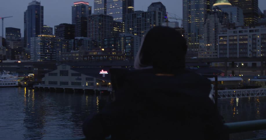 A woman standing on the deck of a boat looks out at the nighttime city skyline