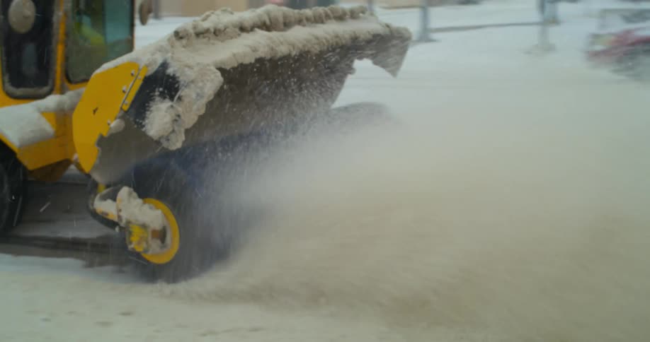 Yellow snow blower vehicle taking the snow out of a street of a big city