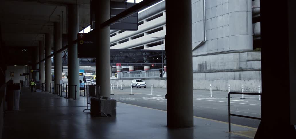 People wait at a bus terminal as cars drive by