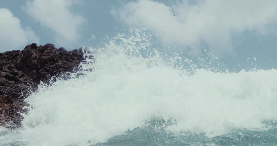 Rough water waves splash against rocks as a wave rolls overhead and the view is now underwater