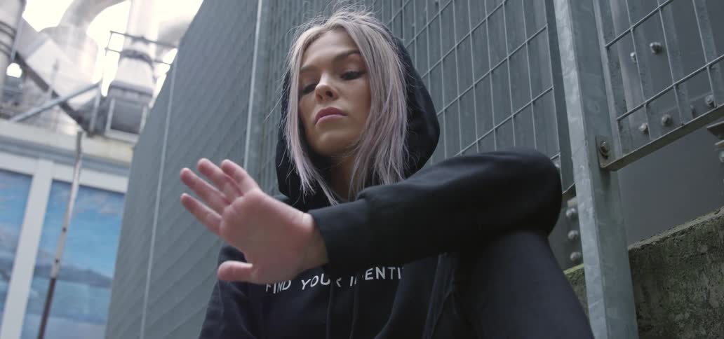 Bored blonde woman wearing a black hoodie sitting on the ground outdoors