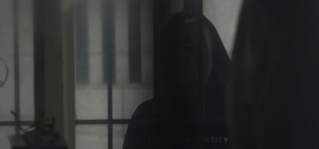 Blonde woman wearing a black hoodie standing behind iron bars and looking ahead