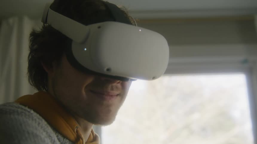 Man with gray sweater equipped with a vr headset uses virtual reality in living room at home