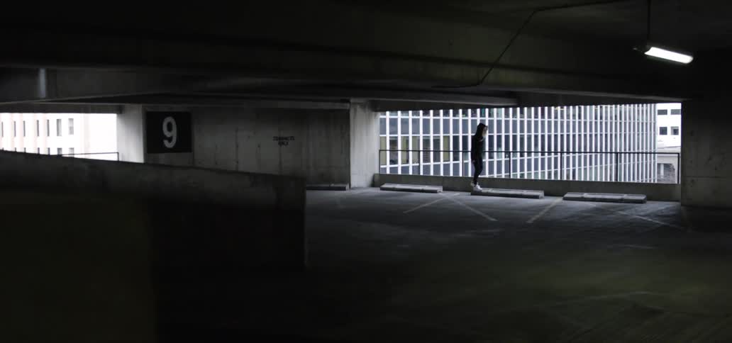 Person wearing a hoodie balances on parking blocks in parking garage