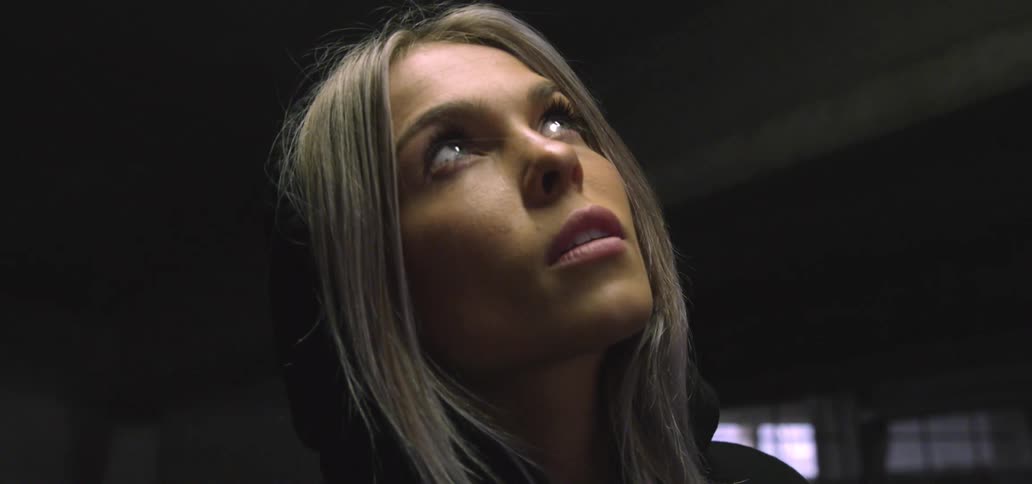 A woman looks up at the ceiling before dropping her gaze to look into the camera