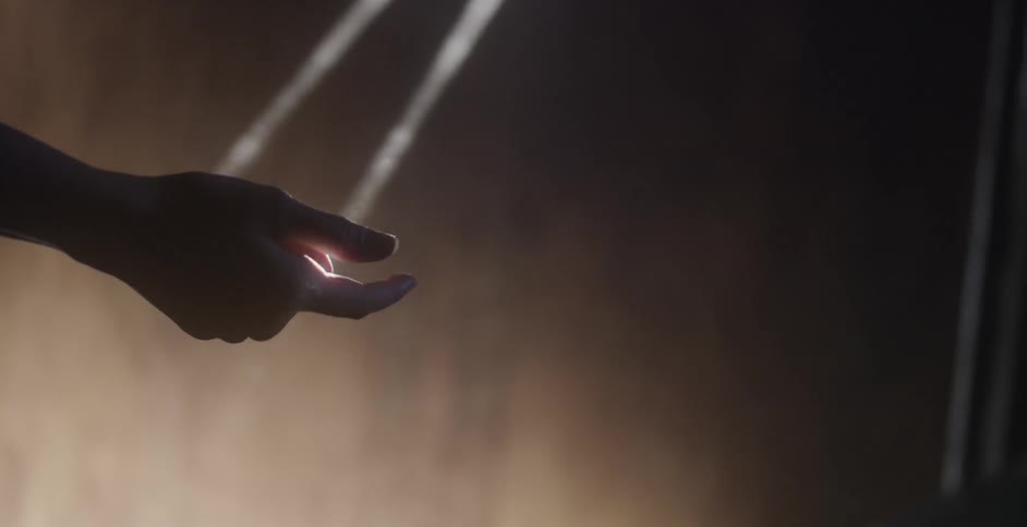 A hand is touching light that is peaking into a dark area