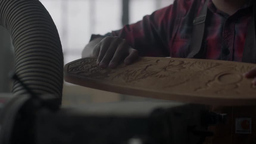 A man sands a piece of carved wood on a sander