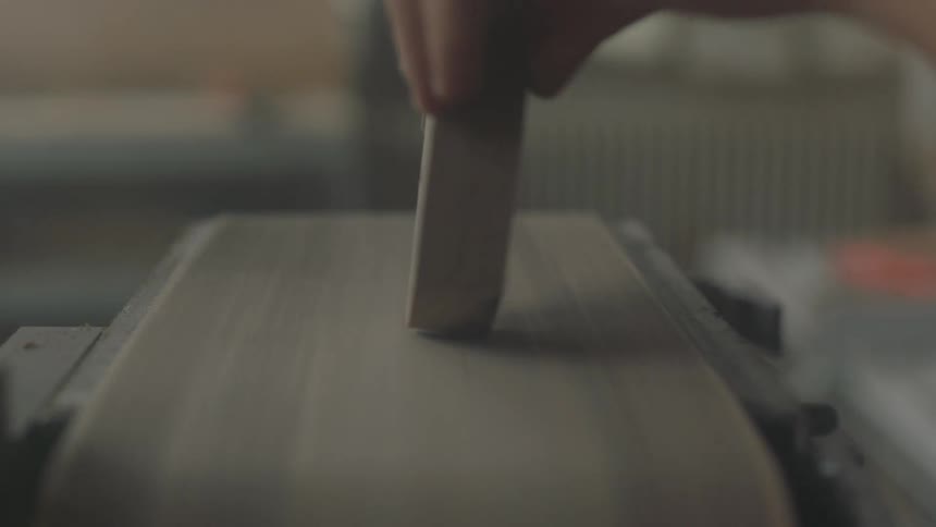 A sanding belt is shaving wood applied by a person