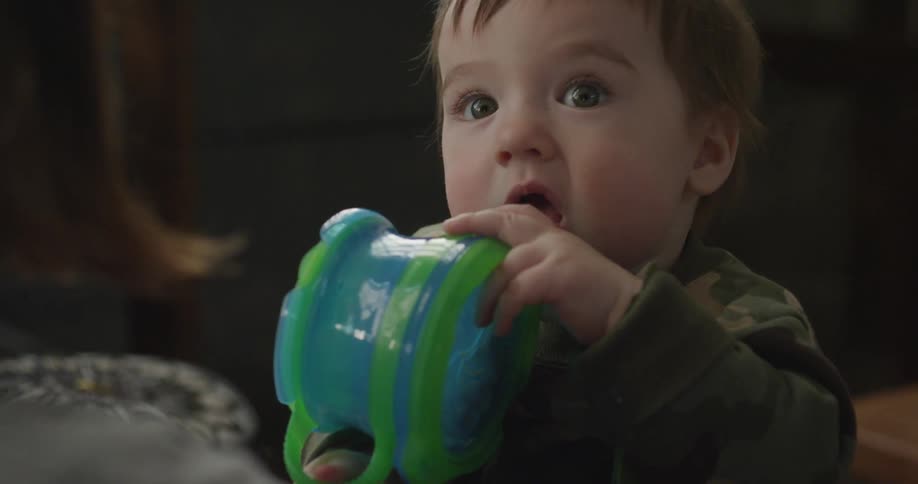 A baby is playing with a blue and green mug