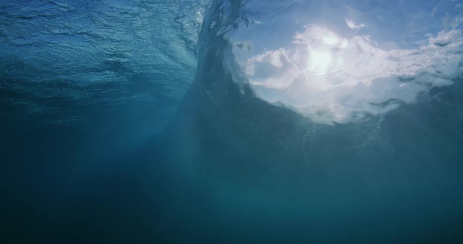 A powerful wave rolls overhead as seen from beneath the surface of the ocean