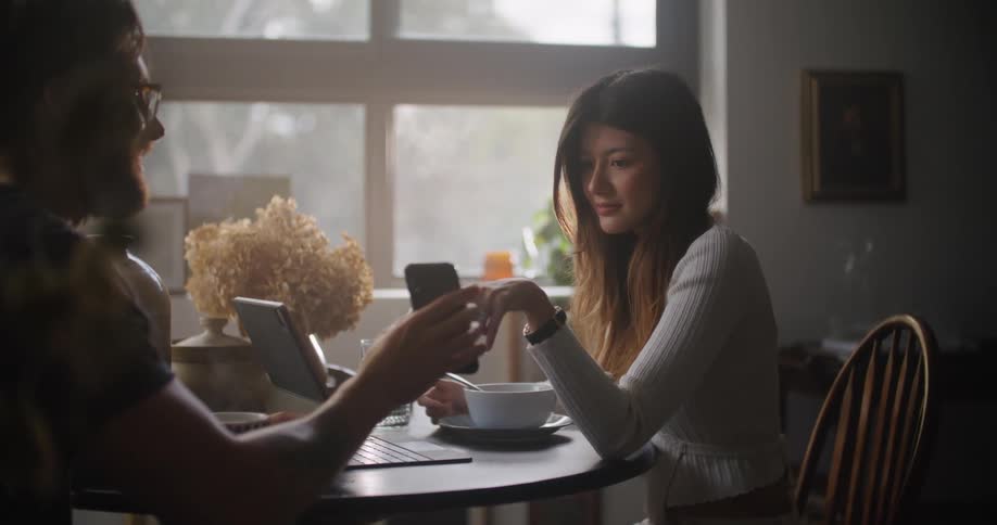 Man sitting at the table next to a woman having a conversation and showing her something on his smartphone