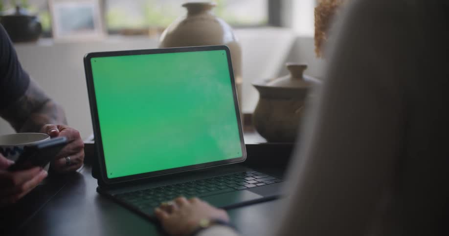 A person uses a laptop while sitting at a table across from a person using a smartphone