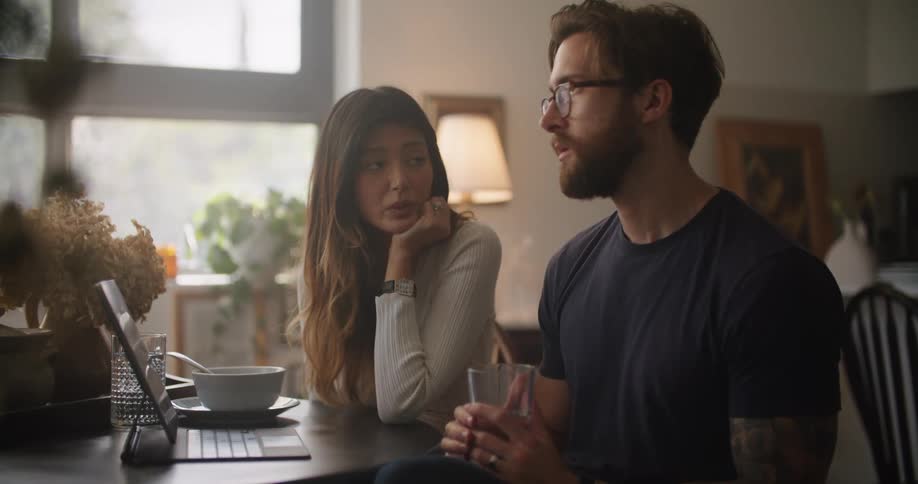 Man and woman sitting at the table talking to each other and looking to a laptop screen