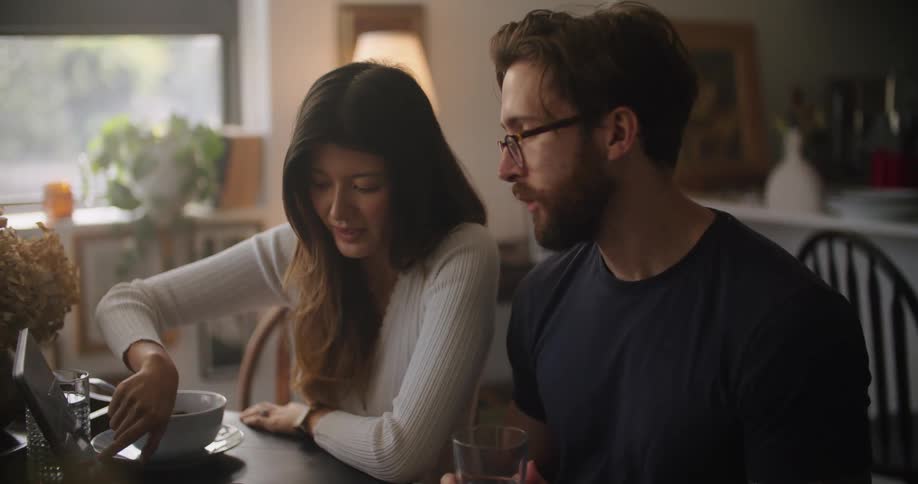 Man and woman sit at a table as they each touch a finger to a laptop screen while they talk