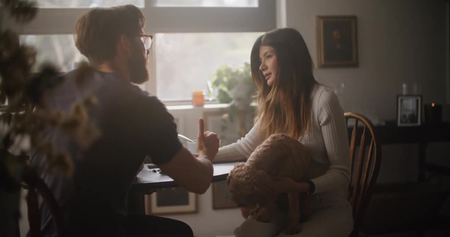 Woman sitting at the table talking to a man and holding a dog on her lap