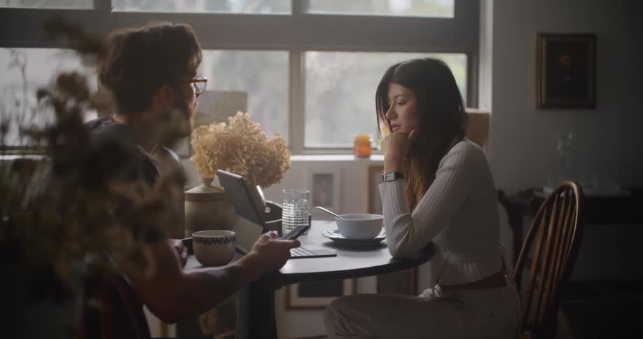 Man and woman sitting at the table talking and using their smartphone and laptop