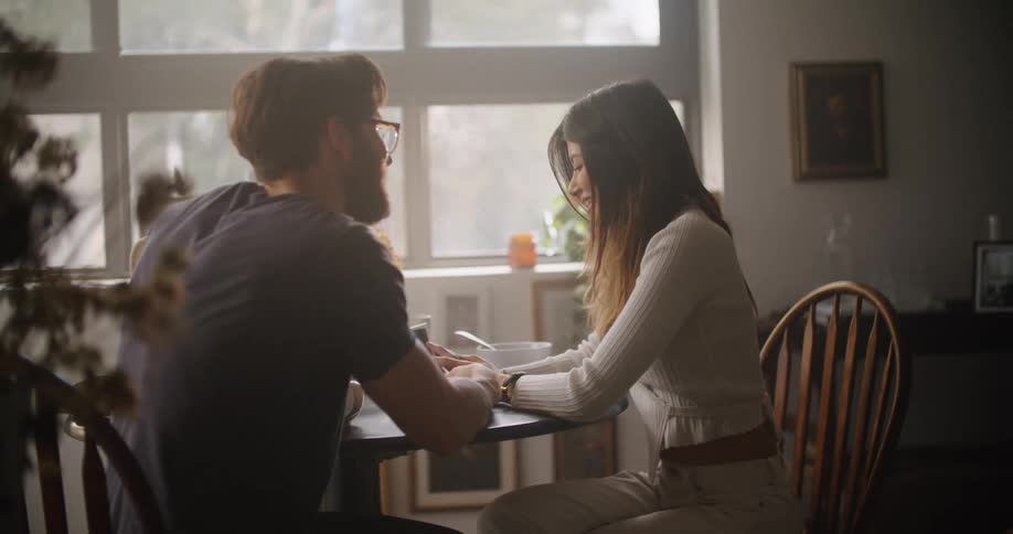A man and woman kissing while sitting at a dining table