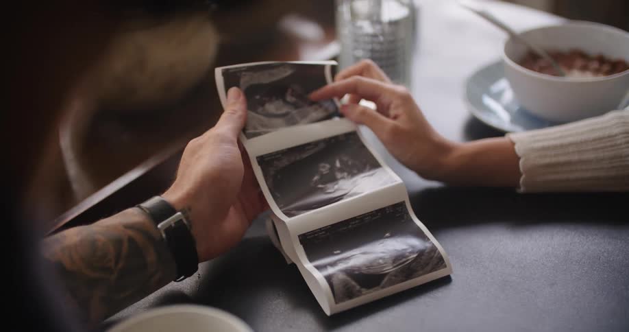 A man and woman examine a roll of sonogram images of a baby in a womb