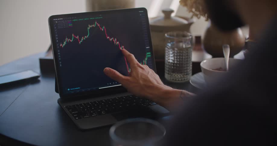 Man and woman sitting at the table looking to and browsing through a candle chart on the laptop screen