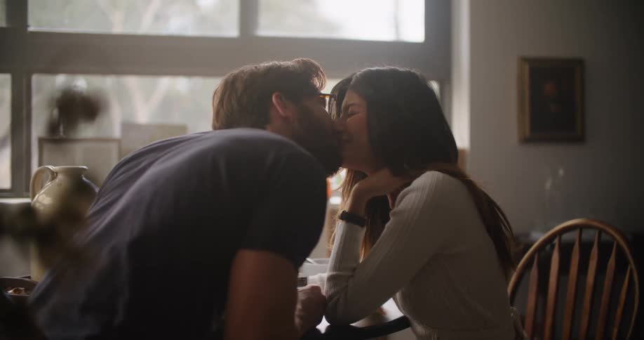 Man sitting at the table shows a printed picture to a woman and kisses her while they both smile