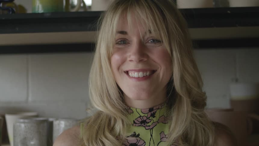 Happy blonde woman wearing green dress with flowers smiling at the camera