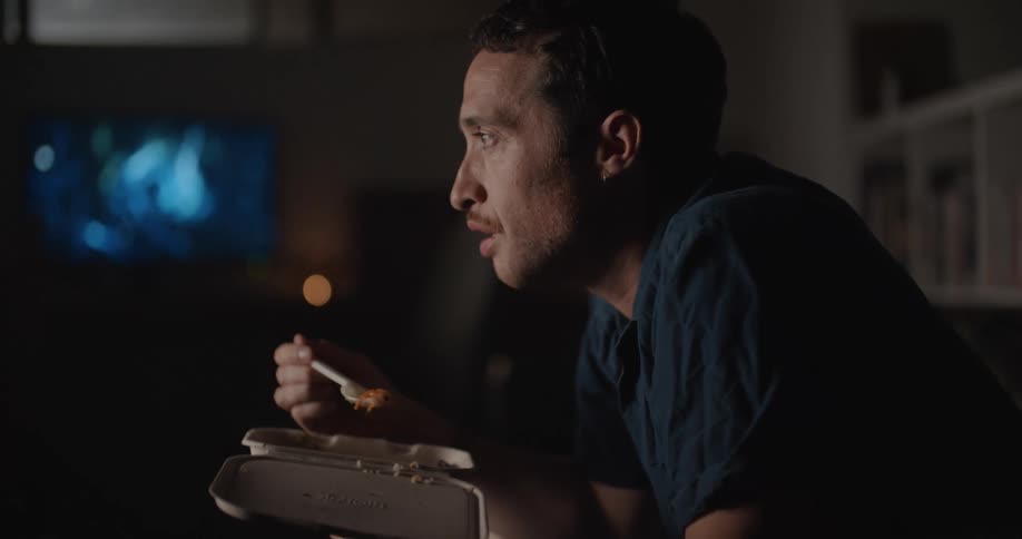 A man sitting in a darkened room pumps his fist in excitement while watching tv
