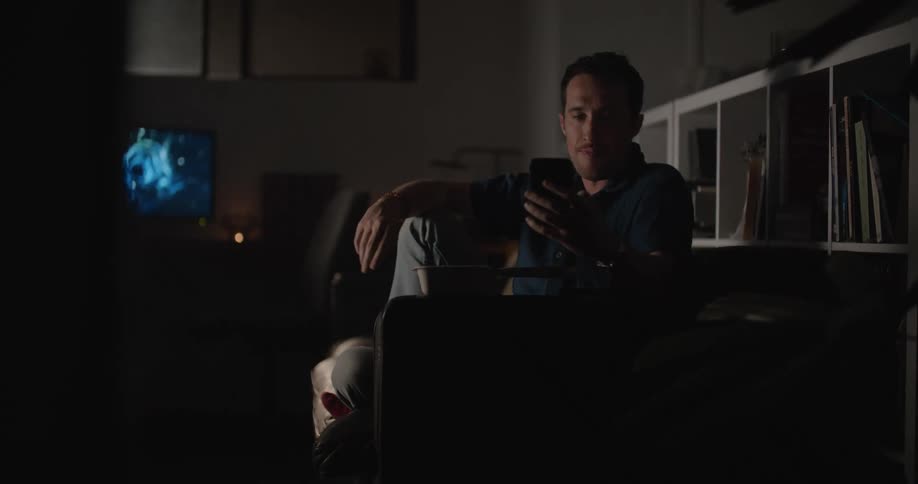 Man sitting on couch eating chinese food while scrolling on social media and watching tv