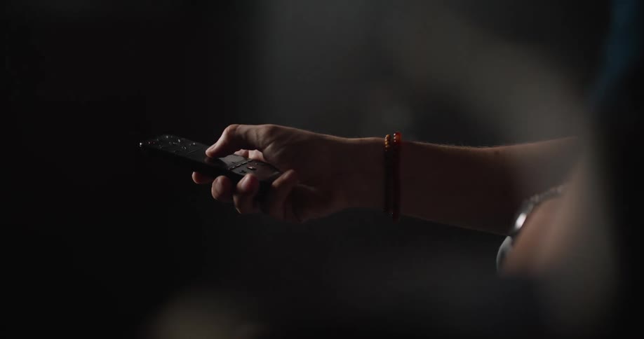 A person wearing a red bracelet using a television remote control