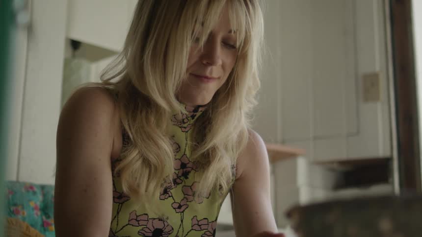 Blonde woman wearing a flowered blouse sculpts a round ball of clay