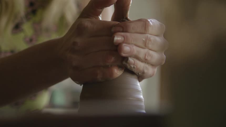 A woman uses her hands to shape a piece of clay that is spinning on a pottery wheel