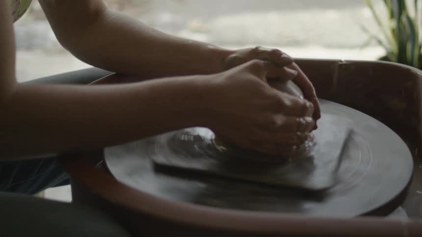 Woman adds water to the clay spinning on a pottery wheel and shapes it with her hands