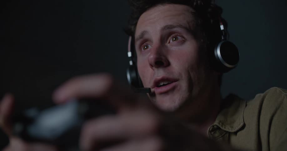 A man talks into his headset while playing video games in a dark room