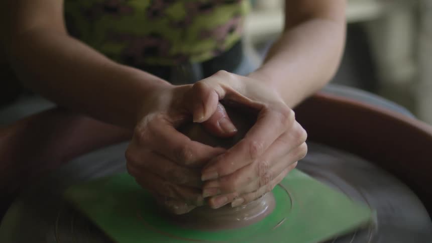 A woman shapes clay on a pottery wheel