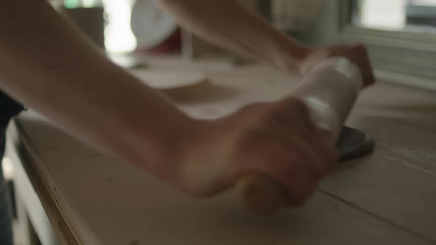 A woman rolling out a disc of clay with a rolling pin