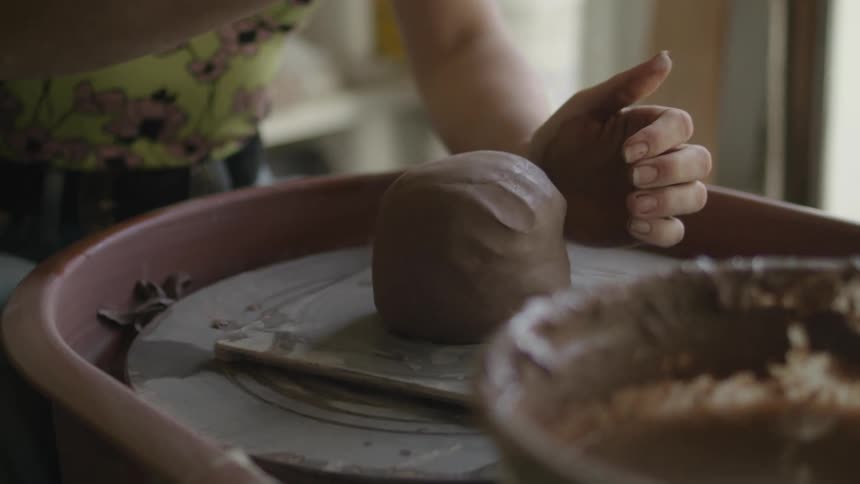 A sculptor dips a cloth in a bucket of water before wringing the cloth to lubricate a ball of clay on a pottery wheel