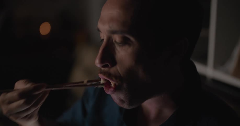 A man scrolling on a phone while eating takeout on a living room sofa