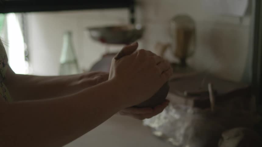 A woman shaping a ball of clay with her hands