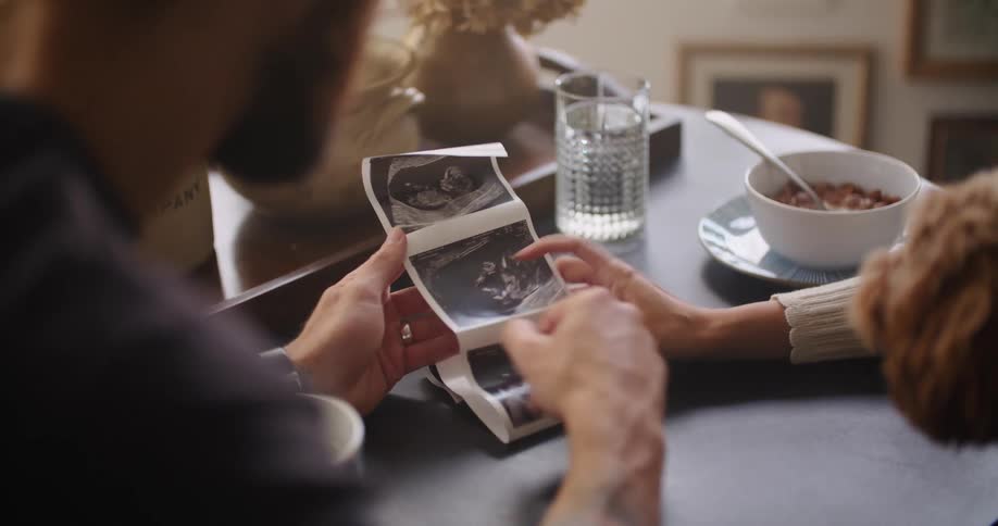 A man and woman sit at their table with their dog and look at ultrasound pictures